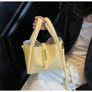 Macro detail of creamy yellow lychee grain leather bucket bag with golden buckle closure