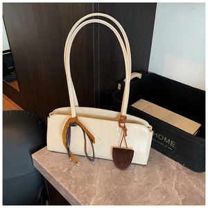 Détail du sac baguette crème avec lanières latérales en cuir et pendentif bouclier
