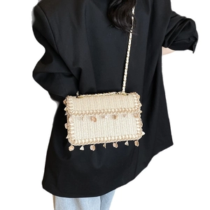 Sac en paille à bandoulière dorée et bordure de coquillages porté par un mannequin