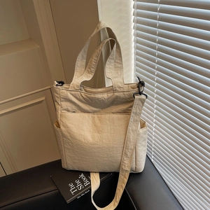 Minimalist beige nylon tote bag with multiple pockets on a stylish leather sofa