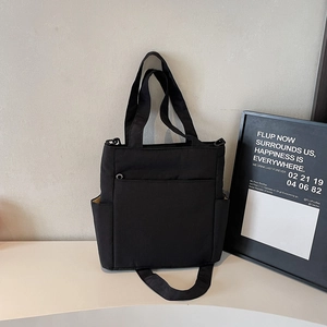 Minimalist black canvas tote bag with front pocket and adjustable shoulder strap