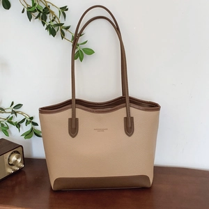 Large capacity contrast leather tote bag with brown trim on a stylish wooden surface