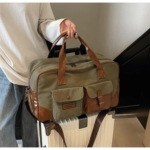 Detail of olive canvas travel bag with brown leather trim placed on a white suitcase