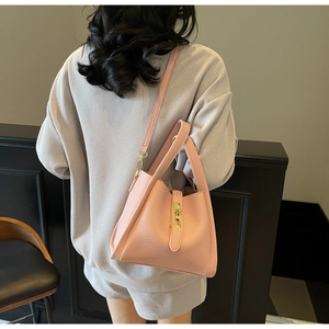 Pink lychee grain leather handbag with gold clasp shown on shoulder from a back side view