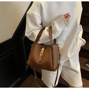 Brown lychee leather bucket bag with gold lock detail and adjustable strap held by model