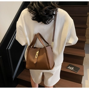 Brown lychee leather tote bag with gold lock shown on model at a modern staircase