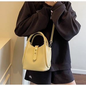 Détail du sac seau en cuir crème avec texture grainée et boucle métallique dorée