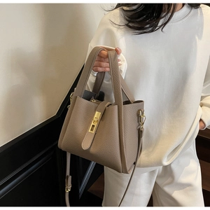 Close-up of taupe litchi grain leather handbag with gold buckle and adjustable strap