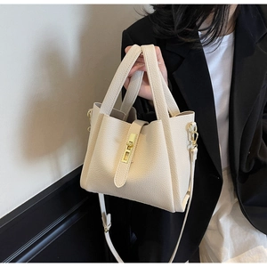 Close-up of cream pebble leather bucket bag featuring a gold twist-lock and top handle