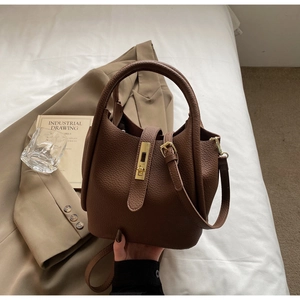 Détail du sac seau en cuir marron foncé à motif litchi avec fermoir doré et bandoulière