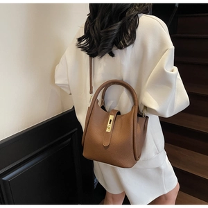 Détail du sac seau en cuir marron grainé avec boucle dorée porté par un mannequin