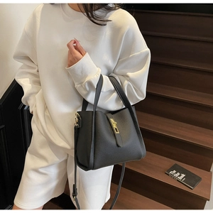 Detail of black pebbled leather crossbody bag with gold buckle on a model