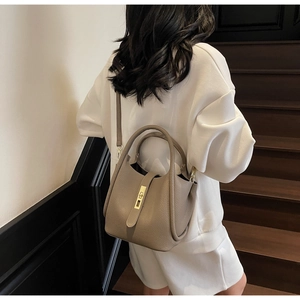 Détail du sac à main en cuir grainé taupe porté avec une tenue blanche chic