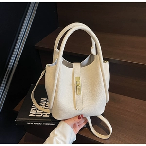 Détail du sac seau blanc à motif litchi avec boucle dorée sur un escalier en bois