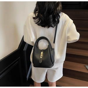 Détail du sac seau en cuir noir avec fermoir doré porté par un mannequin en blanc