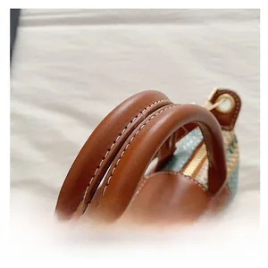 Detail of brown leather handle with white stitching and gold zipper on woven mini bag