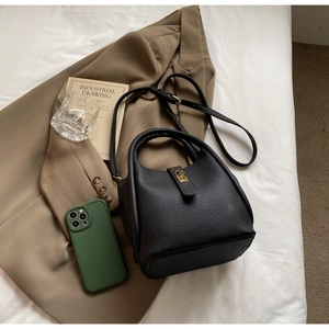 Détail d'un sac seau en cuir noir grainé avec fermoir doré sur une veste marron