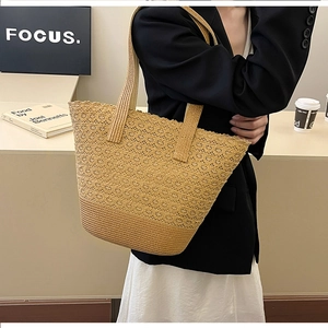 Detail of hollow floral crochet pattern on beige straw tote bag held by model