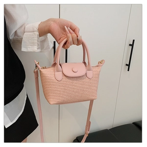 Detail of pink straw woven mini tote bag featuring premium leather handle and flap cover