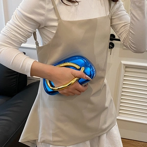 Detail of bright blue mirror finish evening bag with golden round metal handle held by model