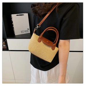 Detailed shot of woven straw handbag featuring brown leather trim and golden metal hardware