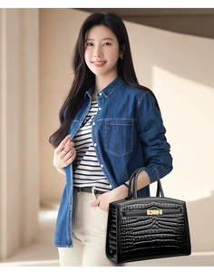 Detail of black crocodile-embossed leather handbag with elegant gold metal lock hardware