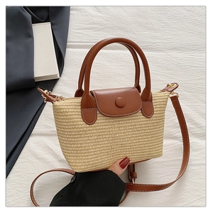 Close-up of woven straw handbag with brown leather flap and white decorative stitching