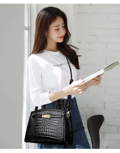 Detail of glossy black crocodile embossed handbag featuring an elegant gold twist lock