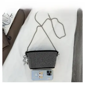 Dettaglio di una mini borsa a secchiello con strass e catena accanto a uno smartphone