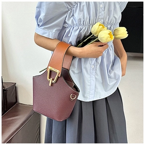 Detail of burgundy bucket bag with contrast brown handle and textured lychee leather