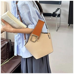 Detail of beige bucket bag featuring orange handles and gold geometric metal buckle