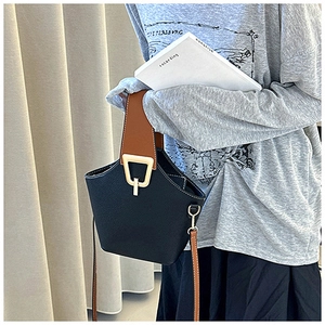 Detail of color-block bucket bag featuring black pebble leather and brown straps with gold buckle
