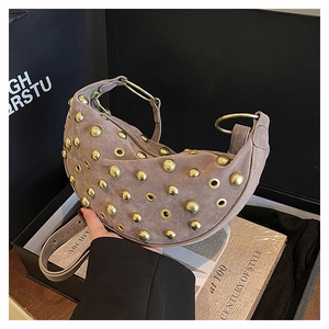 Close-up of suede hobo bag with gold studs and large metal rings on a book background