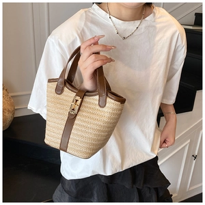 Close-up of woven straw bucket bag with dark brown leather trim and gold metal buckle