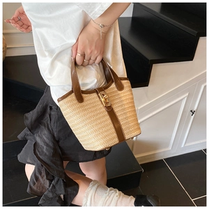Detail of straw bucket bag with brown leather trim and golden metal clasp on stairs