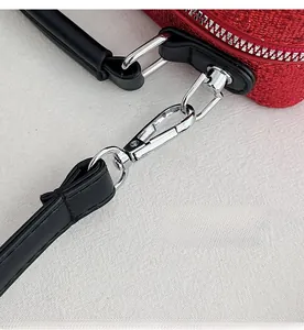 Detail of silver metal hooks and black leather handles on red sequin crossbody bag