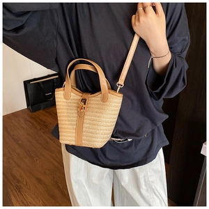 Detail of woven straw bucket bag with brown leather trim and golden metal clasp