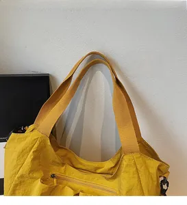 Close-up of mustard yellow nylon tote bag showing wide shoulder strap and front zipper pocket