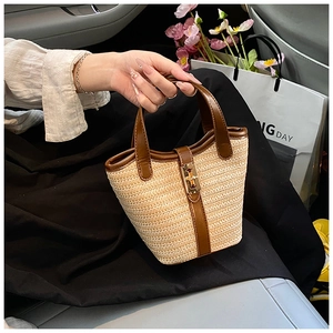 Detail of woven straw bucket bag with dark brown leather handle and gold metal buckle
