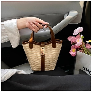 Detail of woven straw bucket bag with brown leather handles and golden metal buckle
