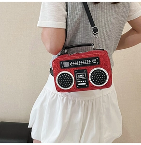 Detail of red glitter radio-shaped crossbody bag worn by a model against a white wall