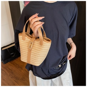 Detail of woven straw bucket bag with brown leather trim and golden twist lock closure