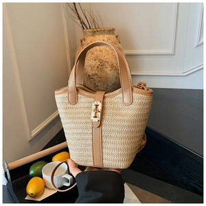 Detail of woven straw bucket bag featuring brown leather trim and golden metal clasp