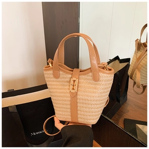 Detail of woven straw bucket bag featuring brown leather trim and golden metal H-clasp