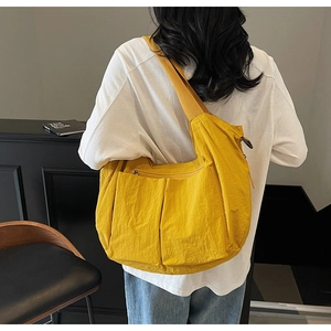 Detail of yellow nylon crossbody bag featuring wide fabric strap and two front pockets