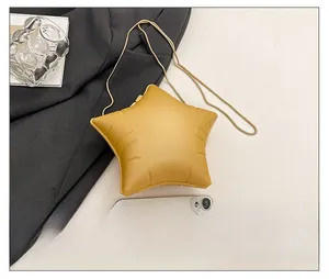 Mini star-shaped crossbody bag in yellow leather with a gold chain strap beside a phone