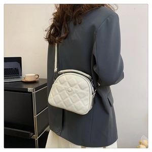 Detail view of cream quilted crossbody bag with top handle and adjustable strap on a model