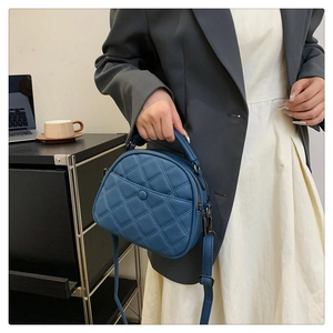 Detail of dark blue quilted crossbody bag with top handle and chain strap on desk
