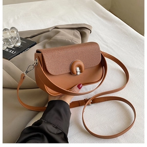 Détail d'un sac bandoulière marron avec rabat tissé et fermoir rotatif en métal doré