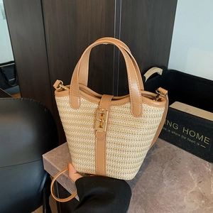 Fashionable straw bucket bag with brown leather trim and golden clasp on marble surface